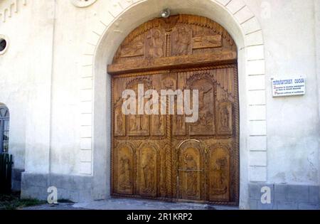 Contea di Tulcea, Romania, 2000. Vista esterna del Monastero di Cocos Cristiano Ortodosso. Le grandi porte d'ingresso in legno, scolpite con scene religiose. Foto Stock