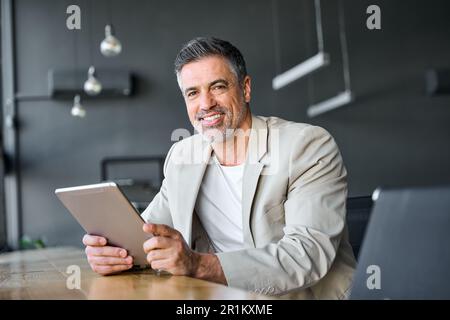 Uomo d'affari di mezza età che tiene un tablet digitale seduto in un ufficio moderno. Verticale Foto Stock