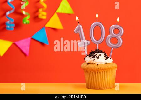 Torta di compleanno con candela numero 108 - sfondo arancione frizzante con bunting Foto Stock