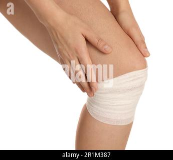 Donna con ginocchio avvolto in bendaggio medico su sfondo bianco, primo piano Foto Stock