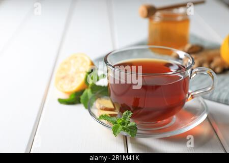 Tazza di delizioso tè allo zenzero e ingredienti su un tavolo di legno bianco, primo piano. Spazio per il testo Foto Stock