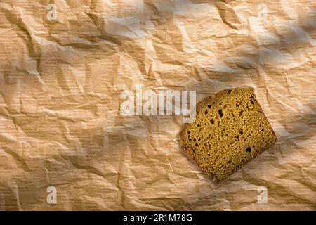 Pane di segale a fette su un fondo marrone isolato. Fette di pane marrone avvolte in carta marrone. Foto Stock