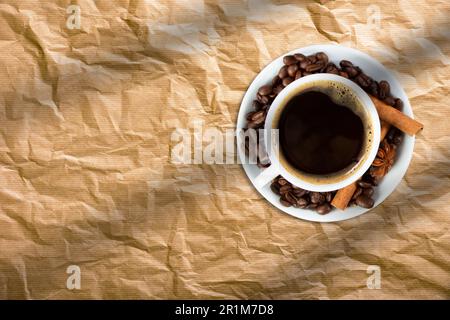 Vista dall'alto di una tazza di caffè, con chicchi di caffè e bastoncini di cannella isolati sulla carta da pane. Foto Stock