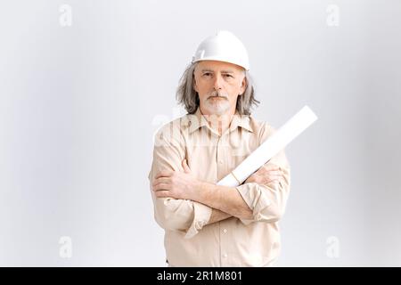 Professionista uomo maturo grigio caucasico con capelli, caposquadra, architetto lavoratore di costruzione in elmetto bianco che tiene il piano architettonico in costruzione, in piedi su sfondo bianco isolato Foto Stock
