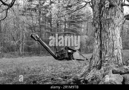 Coppal House Farm - Lee, New Hampshire - Aprile 2023. Un pezzo di attrezzature agricole vintage riposa in un dietro un albero di legno duro esteso in un pascolo. Questo Foto Stock