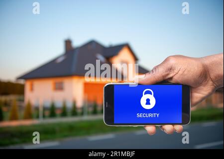 Sistema di sicurezza domestica. Uomo afroamericano con smartphone vicino alla sua casa all'aperto, primo piano Foto Stock