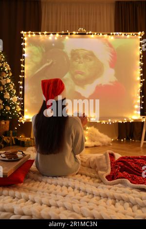 MYKOLAIV, UCRAINA - 24 DICEMBRE 2020: Donna che guarda il film di Grinch tramite videoproiettore in camera. Atmosfera accogliente per le vacanze invernali Foto Stock