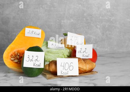 Prodotti alimentari con etichette di potere calorifico su tavola in marmo bianco. Concetto di perdita del peso Foto Stock