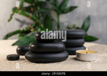 Pietre della stazione termale impilate, bambù e candela sul tappeto di vimini Foto Stock