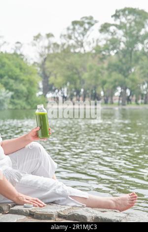 Persona sconosciuta che tiene una bottiglia di succo verde all'aperto. Concetti: Benessere, nutrimento, stile di vita sano e sostenibile. Foto Stock