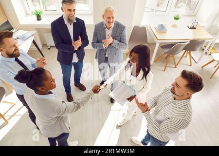 Due donne d'affari si stringono insieme mentre il team d'affari li applaude durante la riunione Foto Stock