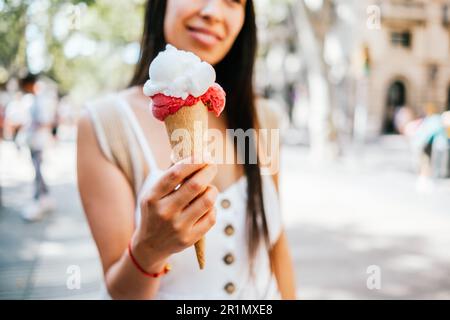 Soft Focus of Crop femmina ispanica dimostrazione cono wafer con gelato nella soleggiata giornata estiva su strada di Barcellona, Spagna Foto Stock