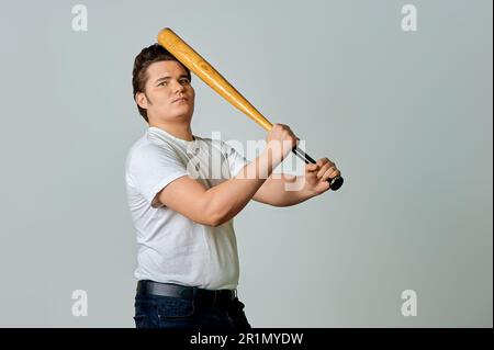 Un uomo con un pipistrello in mano oscilla su uno sfondo grigio Foto Stock