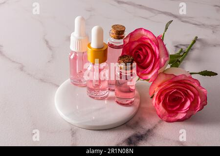 Olio di rosa cosmetico e acqua di rosa in varie bottiglie di vetro su un podio bianco rotondo in marmo con rose. cosmetici naturali. ulteriore cura Foto Stock