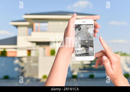 Sistema di sicurezza domestica. Donna che controlla telecamere CCTV su smartphone vicino alla sua casa, primo piano Foto Stock