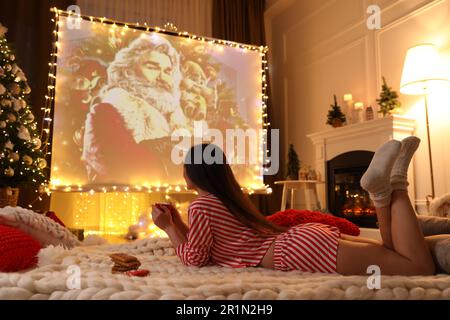 MYKOLAIV, UCRAINA - 24 DICEMBRE 2020: Donna che guarda il film Christmas Chronicles tramite videoproiettore in camera. Atmosfera accogliente per le vacanze invernali Foto Stock