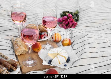 Bicchieri di delizioso vino rosa, fiori e cibo su coperta bianca da picnic Foto Stock