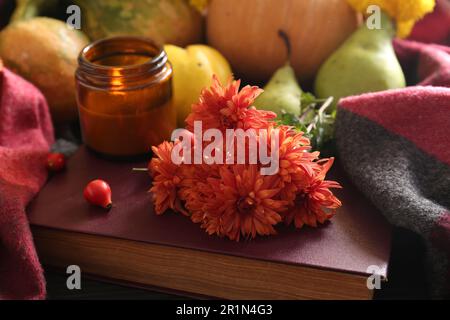 Bei fiori di crisantemo d'arancia, bacche di rosa e candela profumata sul libro. Autunno ancora vita Foto Stock