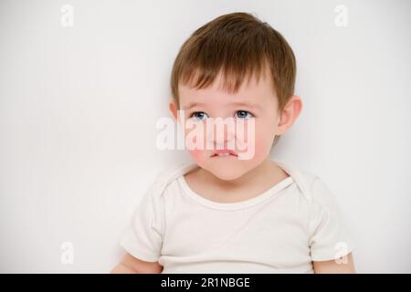 Il bambino offeso guarda le labbra a borsone, studio sfondo bianco. Bambino triste con l'emozione del risentimento sul suo volto. Bambino di circa due anni (un anno nove Foto Stock