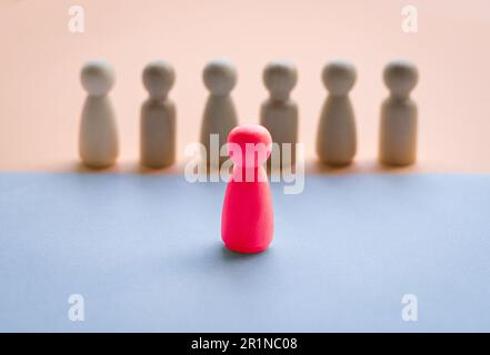 Una bambola di legno rosso che si affaccia su una fila di bambole separate da diversi colori del pavimento. Concetto di leadership. Foto Stock