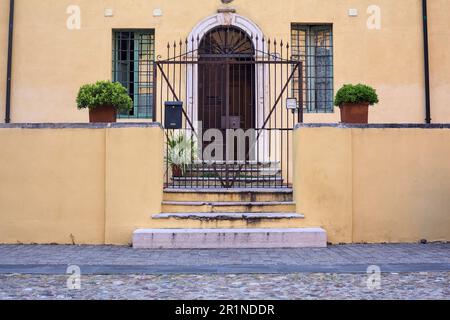 Porta dietro un cancello accanto a una scala in una piazza in una città italiana Foto Stock