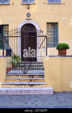 Porta dietro un cancello accanto a una scala in una piazza in una città italiana Foto Stock
