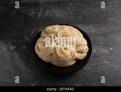 foto pasta bollita giacente in un piatto su uno sfondo scuro Foto Stock