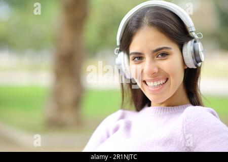 Donna felice con le cuffie ti guarda in un parco sorridente Foto Stock