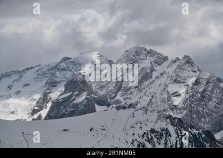 La foto mostra la montagna più grande delle Dolomiti, la Marmolada, con la zona sciistica di fronte, in inverno profondo e le nuvole grigie scure sopra Foto Stock