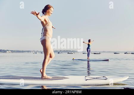 Due donne che fanno yoga sulle tavole SUP la mattina presto Foto Stock