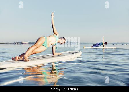 due donne in stand up paddle boarder fare yoga all'alba nella nebbia Foto Stock