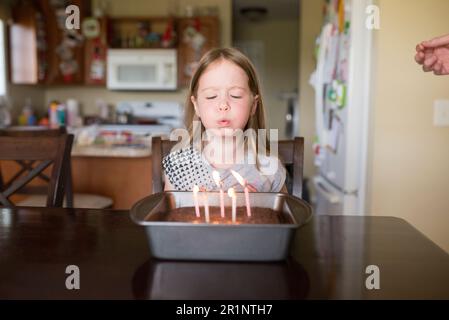 la ragazza di 5 anni soffia le candele sulla torta di compleanno a casa in cucina Foto Stock