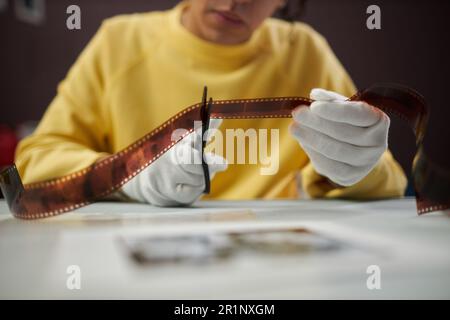 Primo piano del fotografo in guanti bianchi che taglia la pellicola fotografica con le forbici in studio Foto Stock