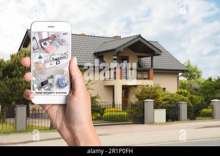 Sistema di sicurezza domestica. Donna che controlla telecamere CCTV su smartphone vicino alla sua casa, primo piano Foto Stock