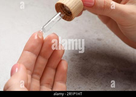 Donna che gocciola siero dalla pipetta sulla sua mano al tavolo grigio, primo piano Foto Stock