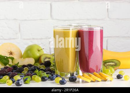 Frullati di frutta freschi e colorati e ingredienti su un tavolo bianco Foto Stock