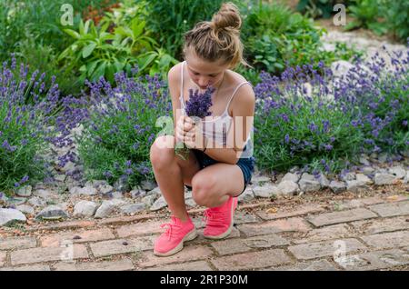 bambino biondo in giardino verde che tiene e profumare fiori di lavanda Foto Stock