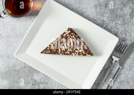 Torta al mosaico al cioccolato con noci su un piatto di porcellana bianca su fondo in pietra Foto Stock