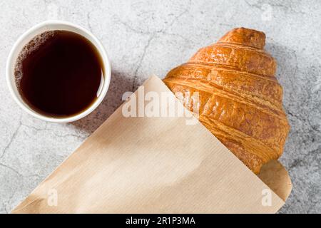 Croissant fresco e delizioso avvolto in carta con tè sul lato Foto Stock