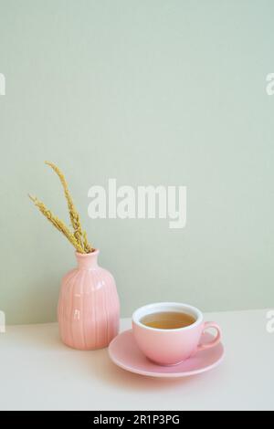 Tazza di tè rosa e vaso di fiore secco su tavola bianca. sfondo parete menta. spazio di copia Foto Stock