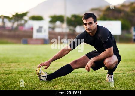 Riscaldarmi prima di giocare. Scatto a tutta lunghezza di un bel giovane sportivo che si allunga da solo prima di una pratica di rugby durante il giorno. Foto Stock