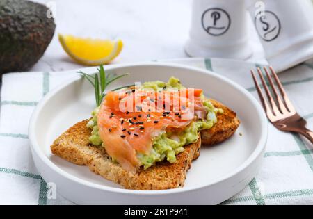 Brinda con avocado e salmone affumicato cosparso sulla parte superiore con semi di sesamo a vista ravvicinata del tavolo di marmo - mangiare sano Foto Stock