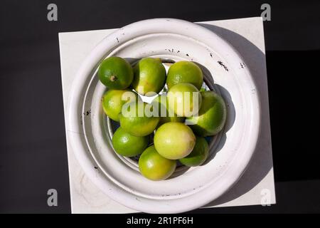Bacinella di frutta piena di lime verdi su una vista da tavolo bianca come elemento decorativo interno. Natura morta artistica astratta con elementi geometrici, luce Foto Stock