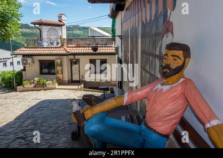 Intaglio in legno a grandezza naturale di un uomo del posto seduto su una panchina di strada e bevendo una birra, in una strada a Veliko Tarnovo, Bulgaria. Foto Stock