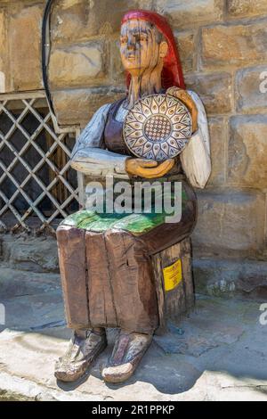 Intaglio in legno a grandezza naturale di una donna locale che tiene un piatto progettato tradizionalmente, seduto in una strada a Veliko Tarnovo, Bulgaria. Foto Stock