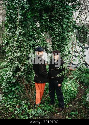 Coppia non binaria di fronte al muro con graffiti Foto Stock