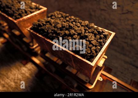 Sette vecchi carri da miniera o carrelli pieni di carbone che si muovono lentamente attraverso il passaggio stretto. Tunnel sotterraneo scuro pieno di curve con trac ferroviario Foto Stock