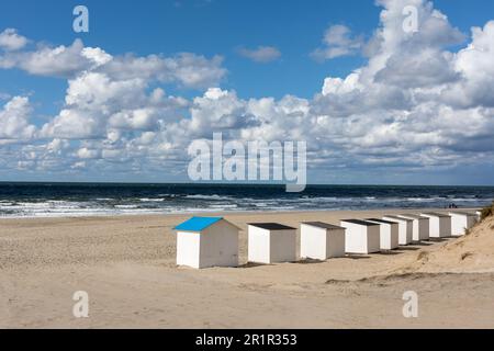 Una splendida scena di capanne sulla spiaggia allineate sullo sfondo di ondulate dune di sabbia sulla costa Foto Stock