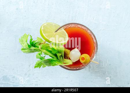 Cocktail Bloody Mary con contorno, shot piatto sospeso. Un bicchiere di succo di pomodoro piccante con alcol, lime, sottaceti e sedano Foto Stock