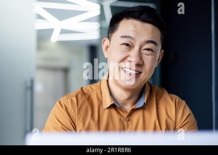Primo piano. Ritratto di giovane uomo d'affari asiatico sorridente in camicia in ufficio moderno. Foto Stock